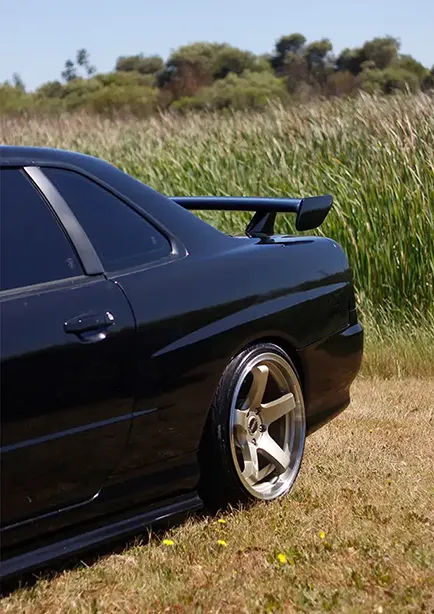 Rear side shot of a black Nissan Skyline R34 near a farm